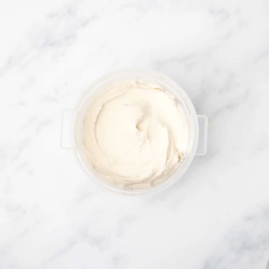 A plastic container filled with smooth, pale dough resting on a white marble surface.