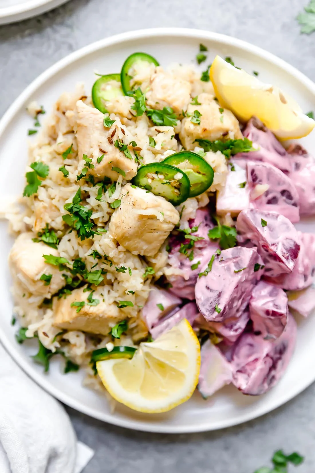A plate of chicken pulao topped with sliced chiles and lemon wedges