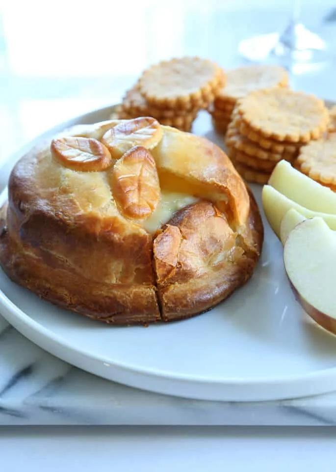 A plate with a close up of Brie en Croute, apple slices and crackers in back