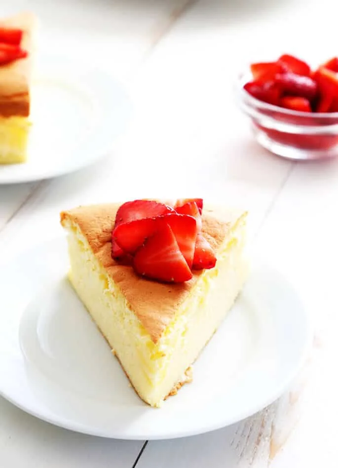 A slice of Japanese cheesecake with strawberries on top on a white plate