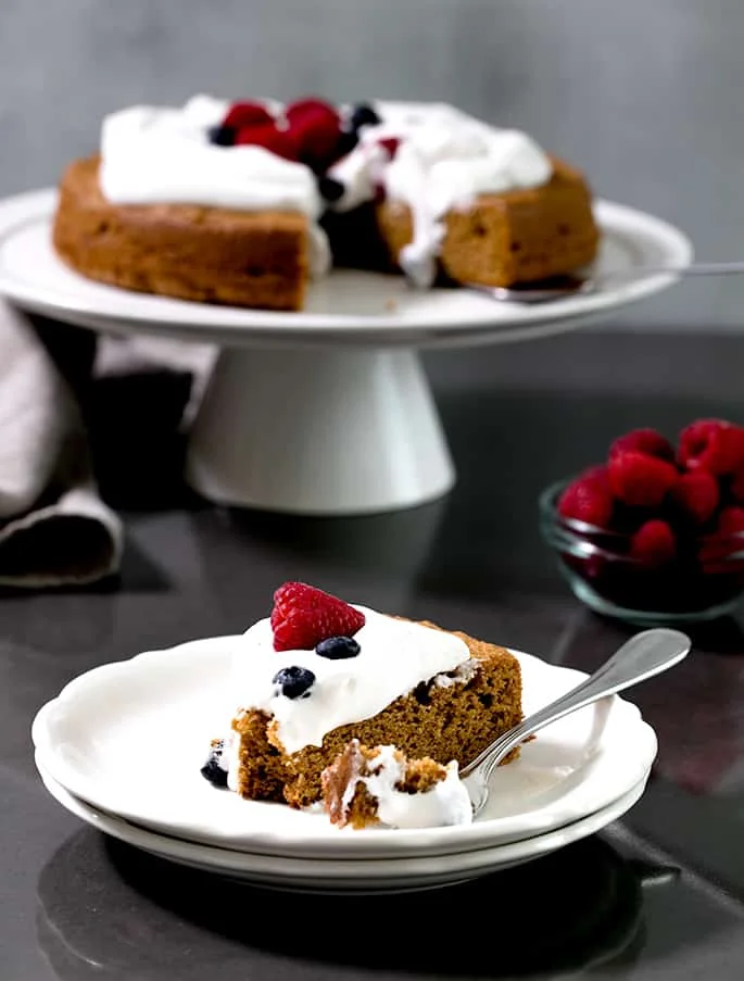 A slice of the finished cake served on a white plate with the rest of the cake on a stand in the background.