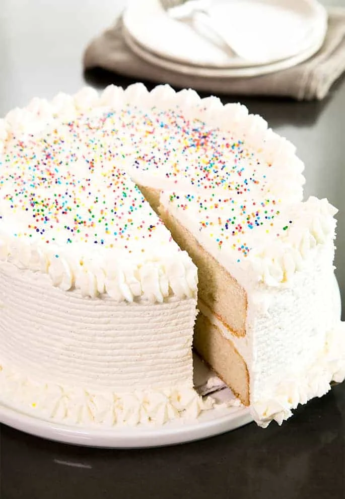 A slice of vanilla cake being taken from a cake with vanilla ermine frosting