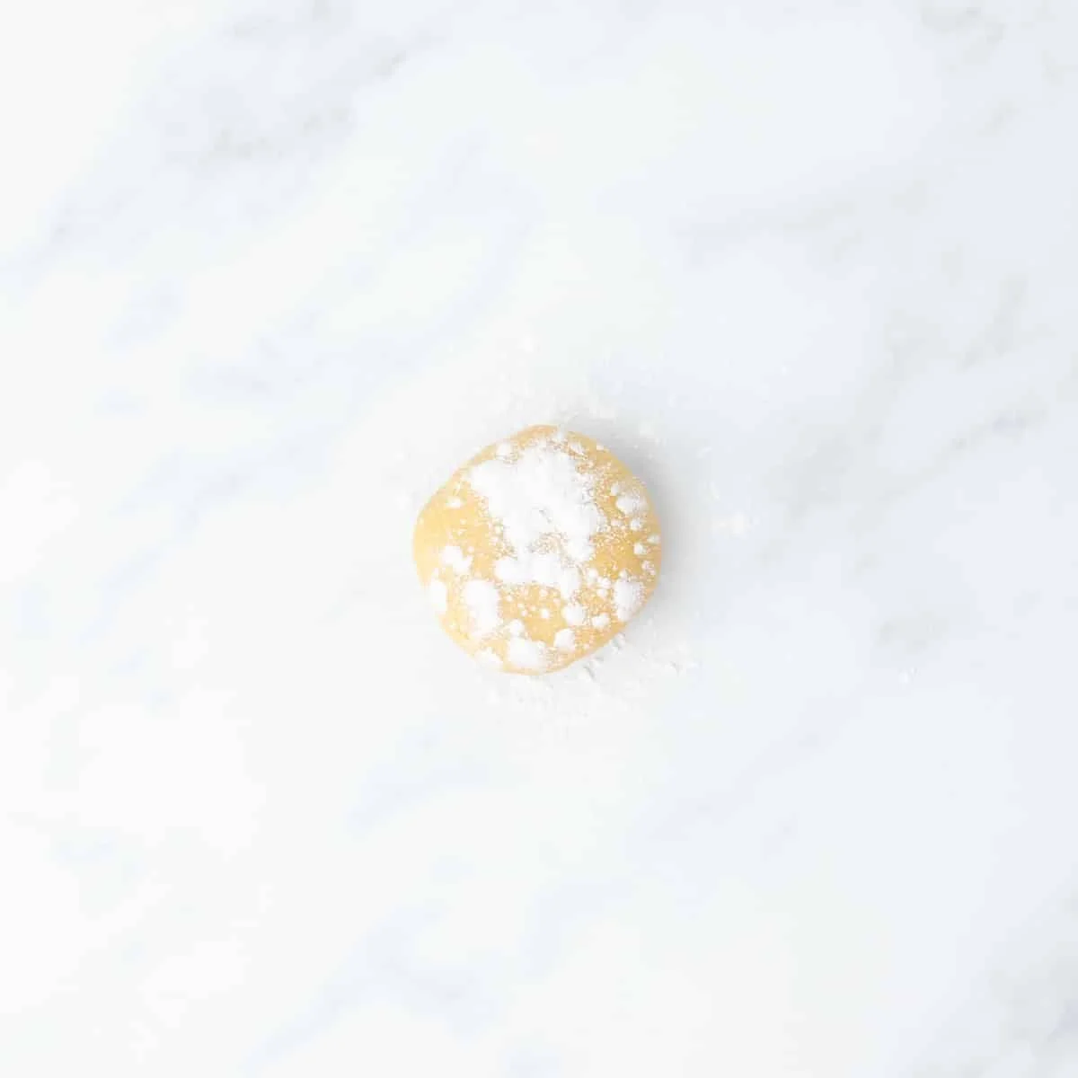 A small ball of dough dusted with gluten free flour, resting on a white marble surface.