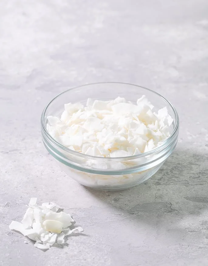 A small glass bowl with white coconut flakes on a gray background