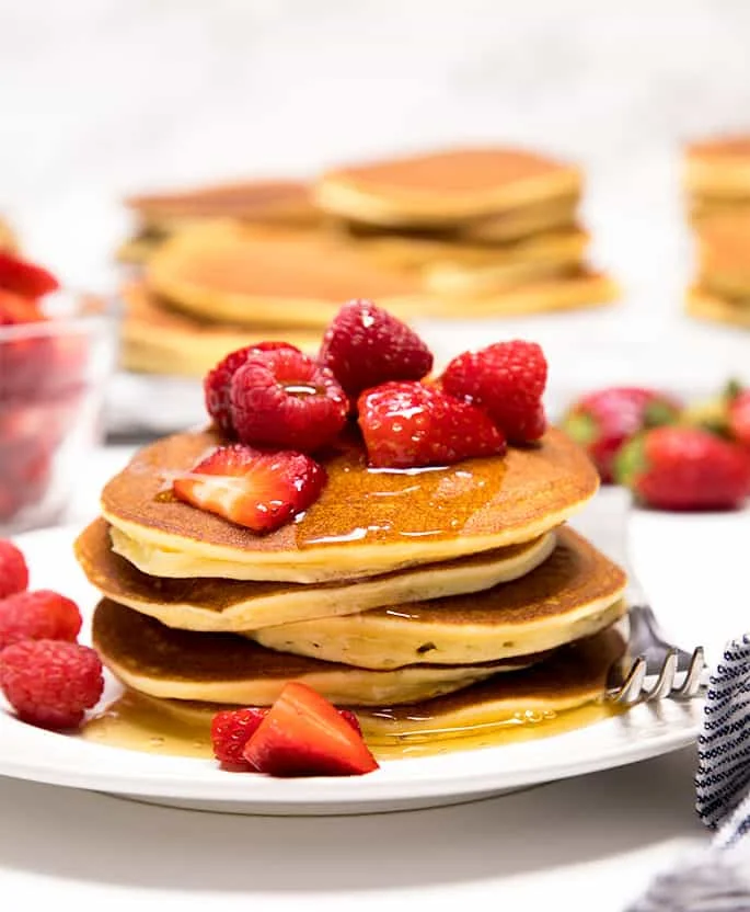 A stack of coconut flour pancakes with honey and fruit on a plate