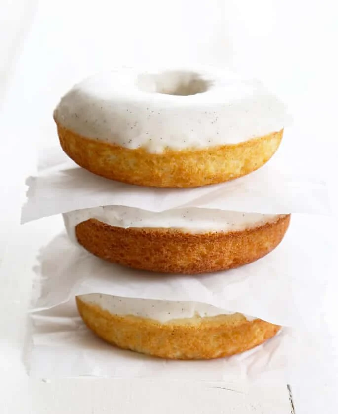 A stack of three vanilla cake donuts with white glaze