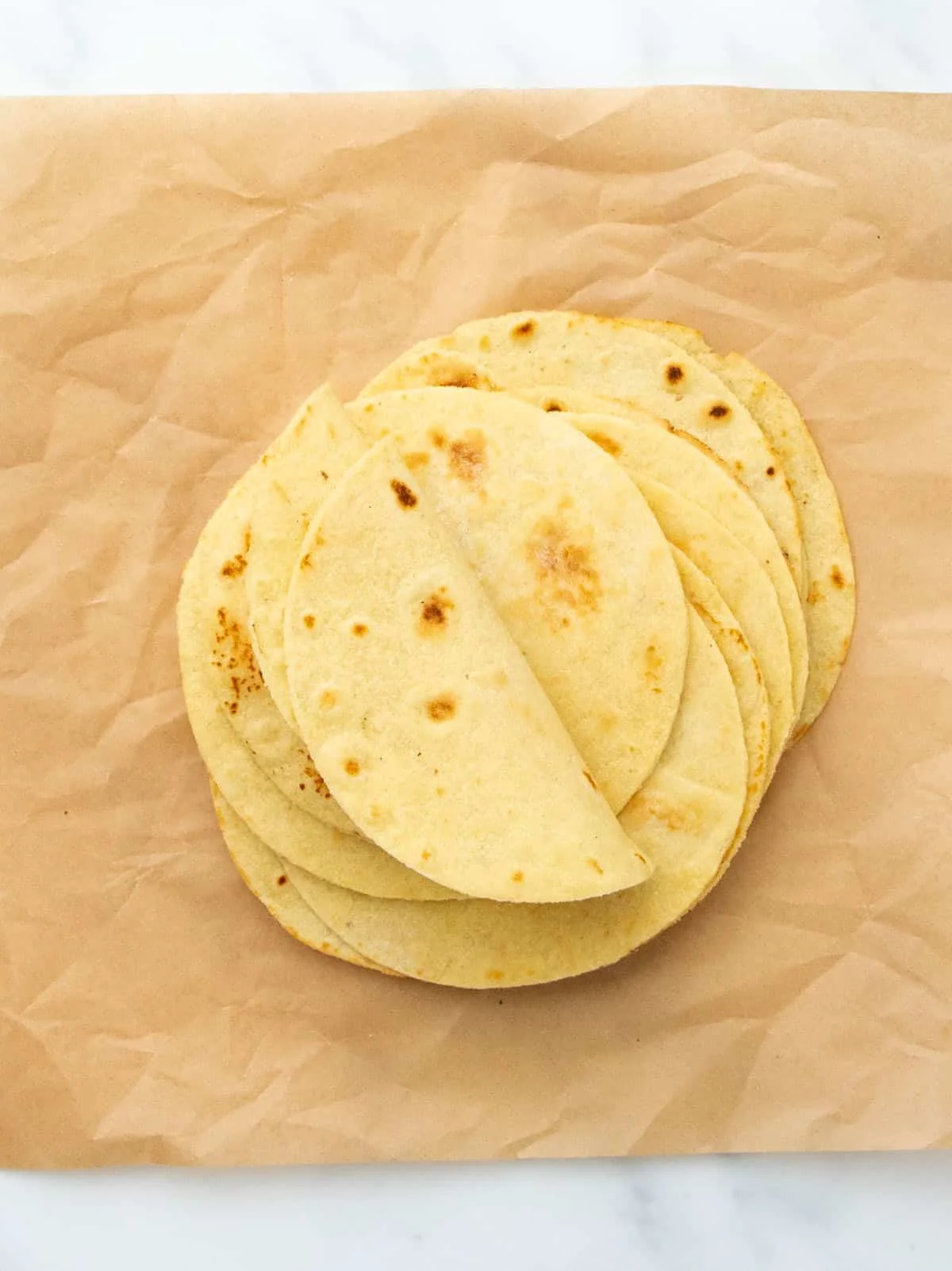 A stack of tortillas on brown parchment paper with a few edges folded upward.