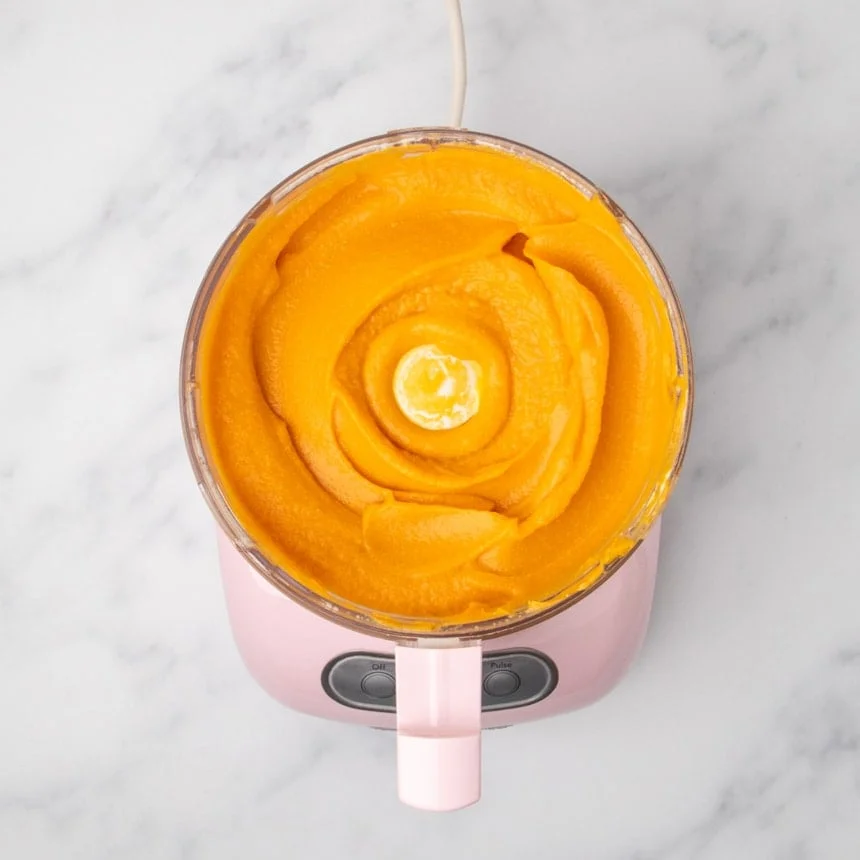 A top view of a food processor filled with smooth orange sweet potato mixture.