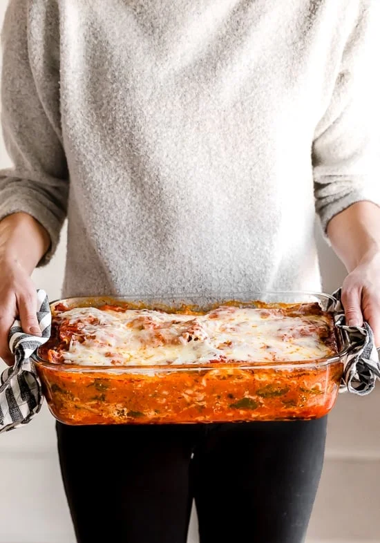 A woman holding a casserole dish of chicken parmesan lasagna