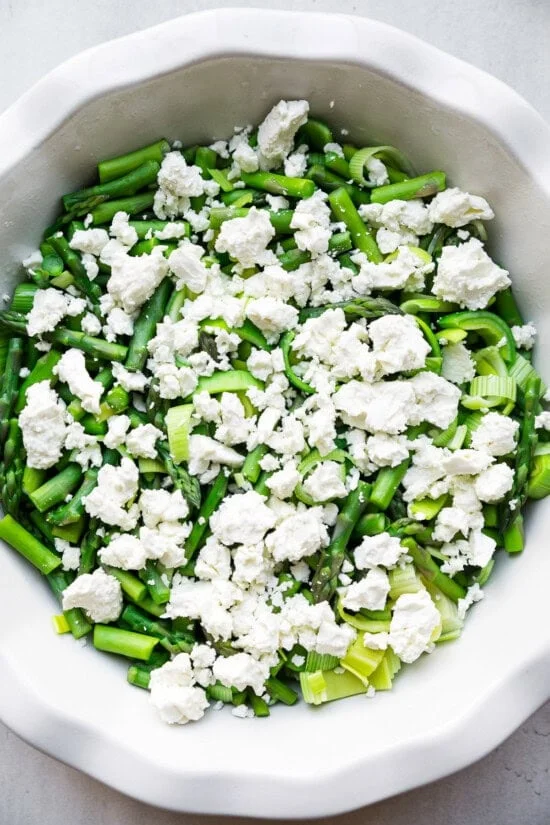 Add veggies and feta to a quiche dish.