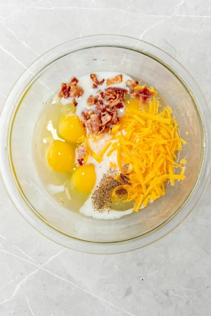adding all of the ingredients needed to make egg bites into a glass bowl 