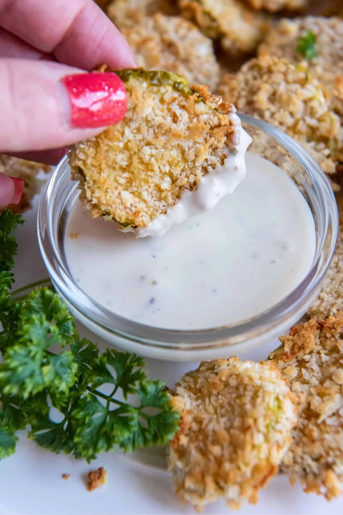 Air fried pickles on a serving plate, with one being held in a hand and being dipped into a sauce.
