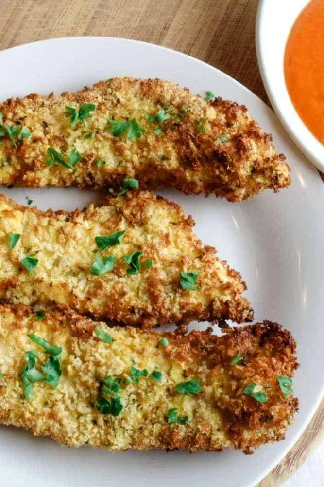 Air Fryer Chicken Tenders with breading and parsley on a white plate with buffalo sauce in a white pinch bowl in corner