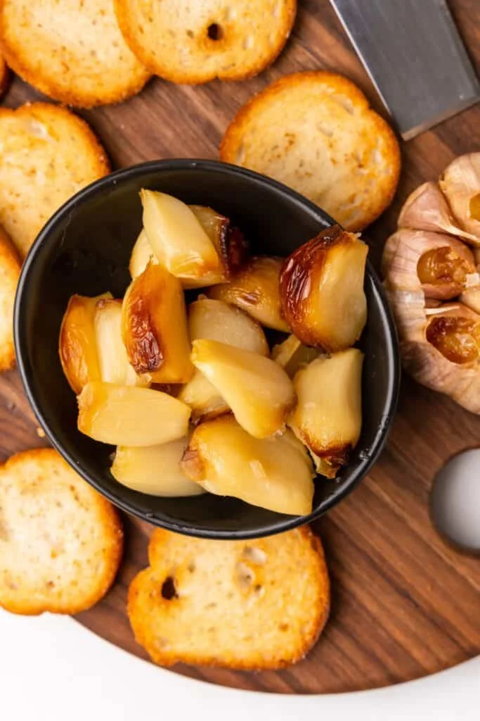 Air fryer roasted garlic peeled out of the shells, served in a bowl with crostini pieces to be spread on top of them.