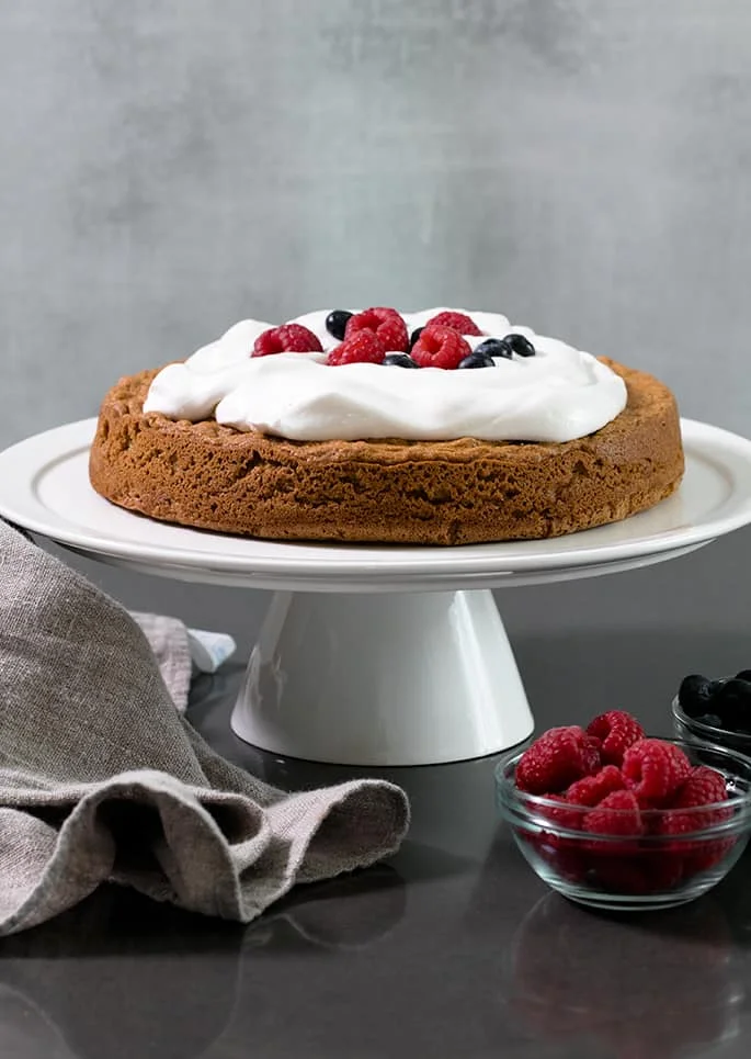 Almond flour sponge cake with whipped cream and berries on a platter.