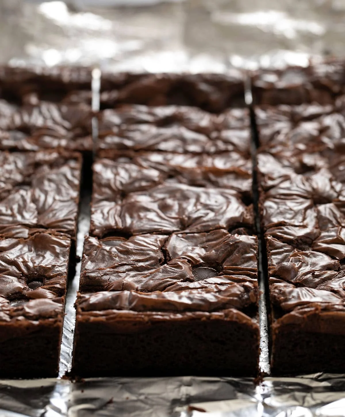 An image of sliced square flourless brownies on aluminum foil
