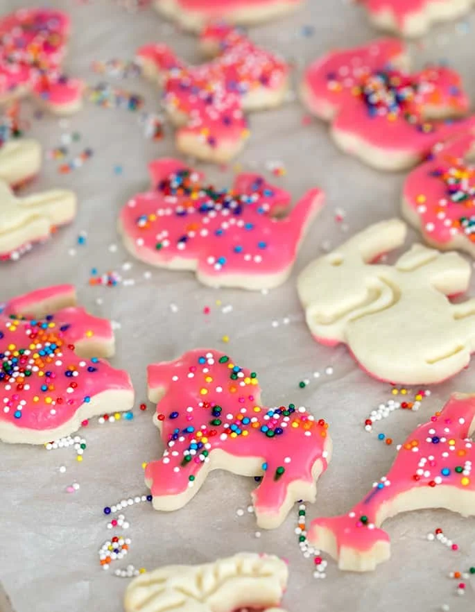 Animal cracker cookies with pink frosting and rainbow nonpareils on white paper.