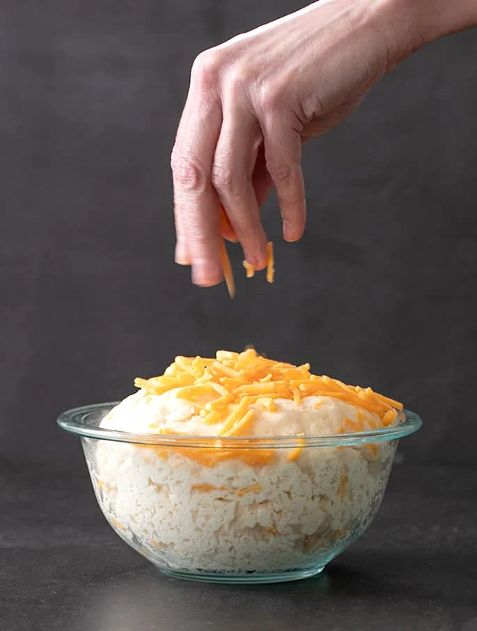 Artisan cheese bread raw risen dough being sprinkled with more cheese