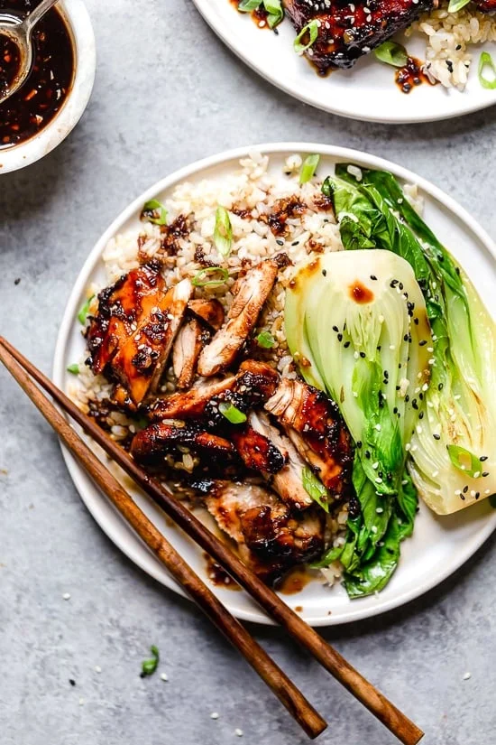 Asian Chicken Thighs on a plate with rice and chop sticks.