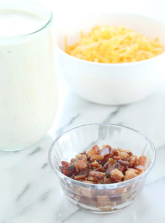 Bacon bits in a bowl and cheese in a white bowl on a marble surface