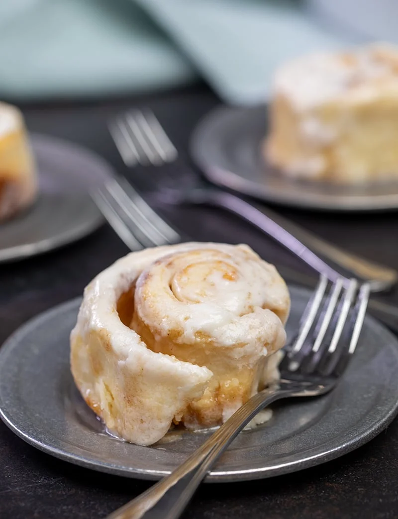 Baked and frosted rolls on small round metal plate with fork.