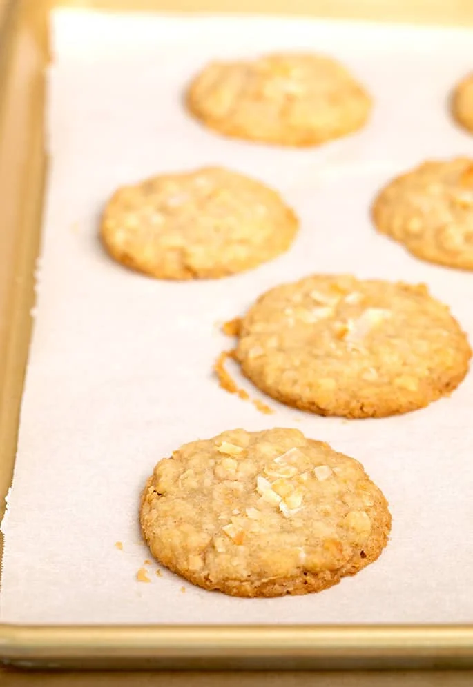 Baked coconut cookies on right side of tray lined with white paper