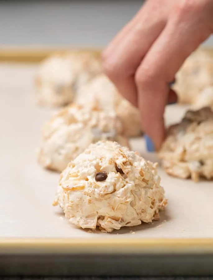 Baked coconut macaroons on white paper on baking tray with fingers in background