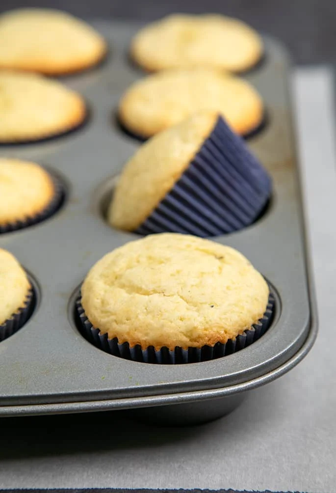 Baked cupcakes in blue liners in muffin tin on white paper.