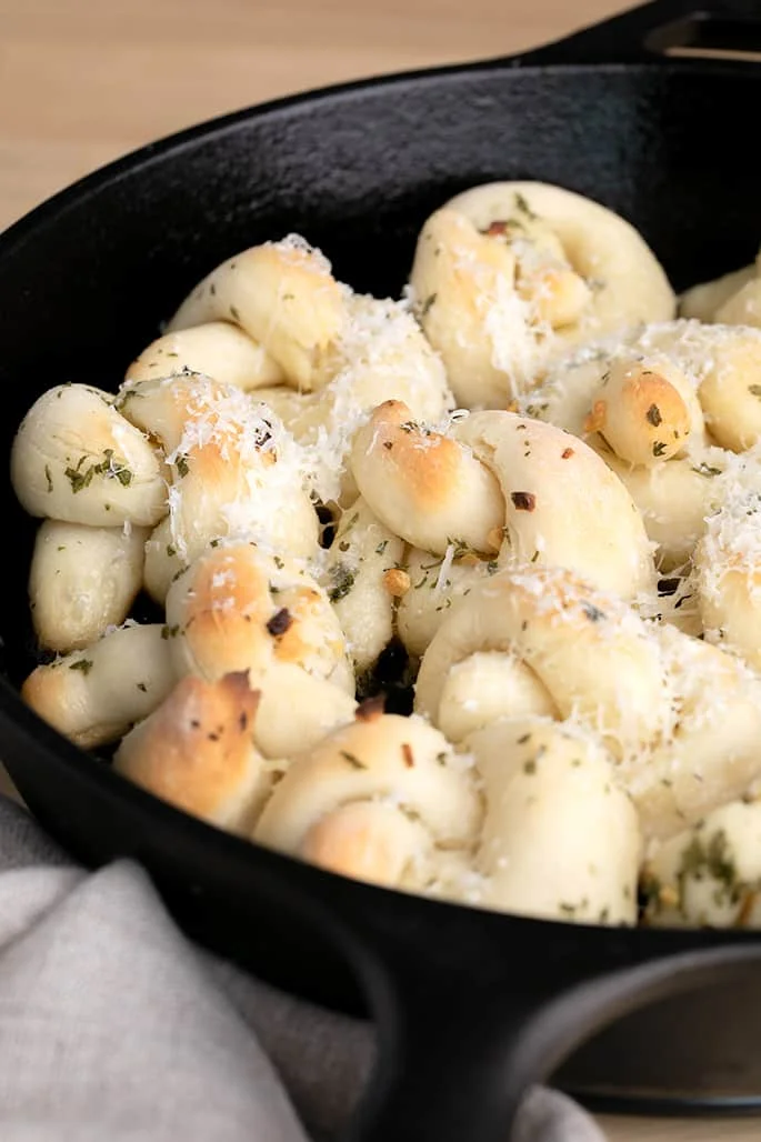 Baked garlic knots with finely grated parmesan in black skillet