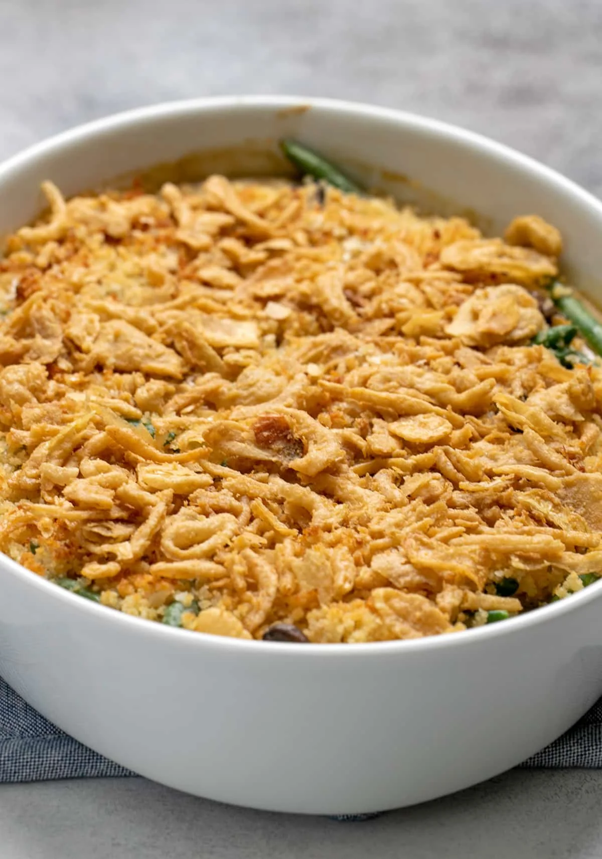 Baked green bean casserole with crispy fried onions on top in white casserole dish on blue potholder