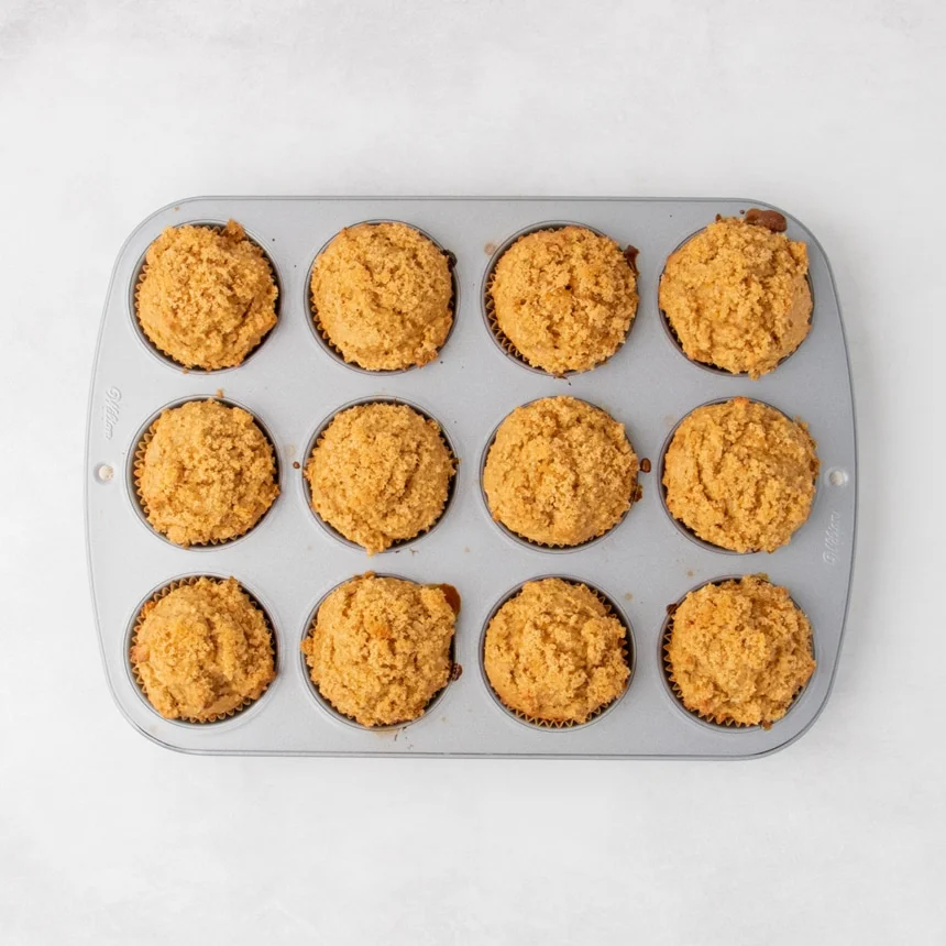 Baked muffins in a 12-cup muffin pan, with golden tops and texture of craggy brown sugar topping visible.