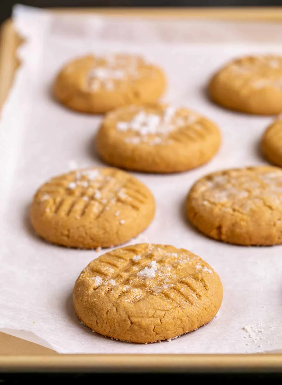 Baked peanut butter cookies on white paper on gold rimmed baking sheet