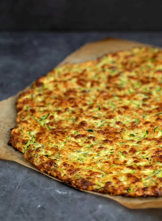 Baked yellow and green zucchini pizza crust without toppings on brown paper