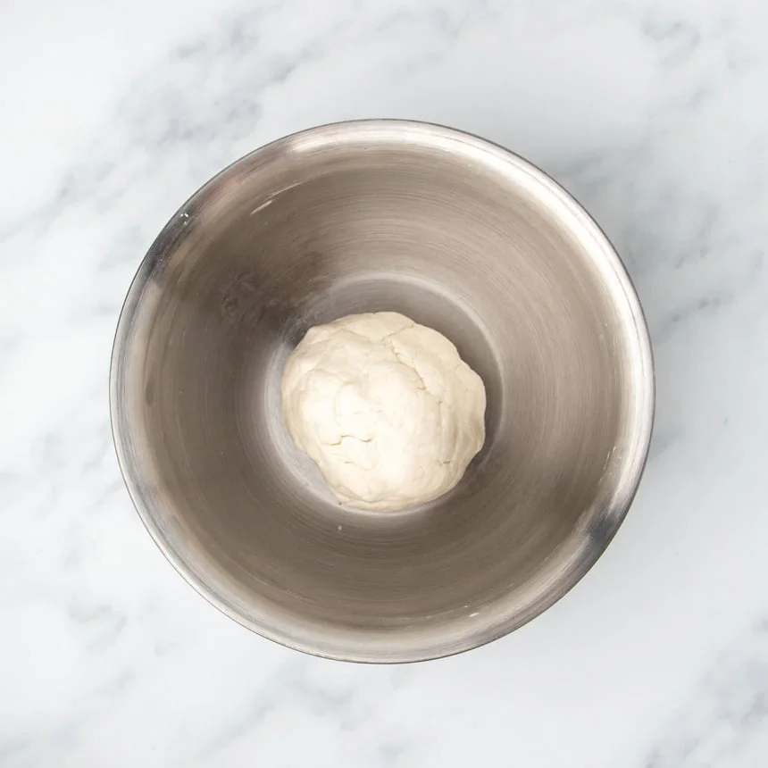ball of very light tan colored raw tortilla dough resting in mixing bowl