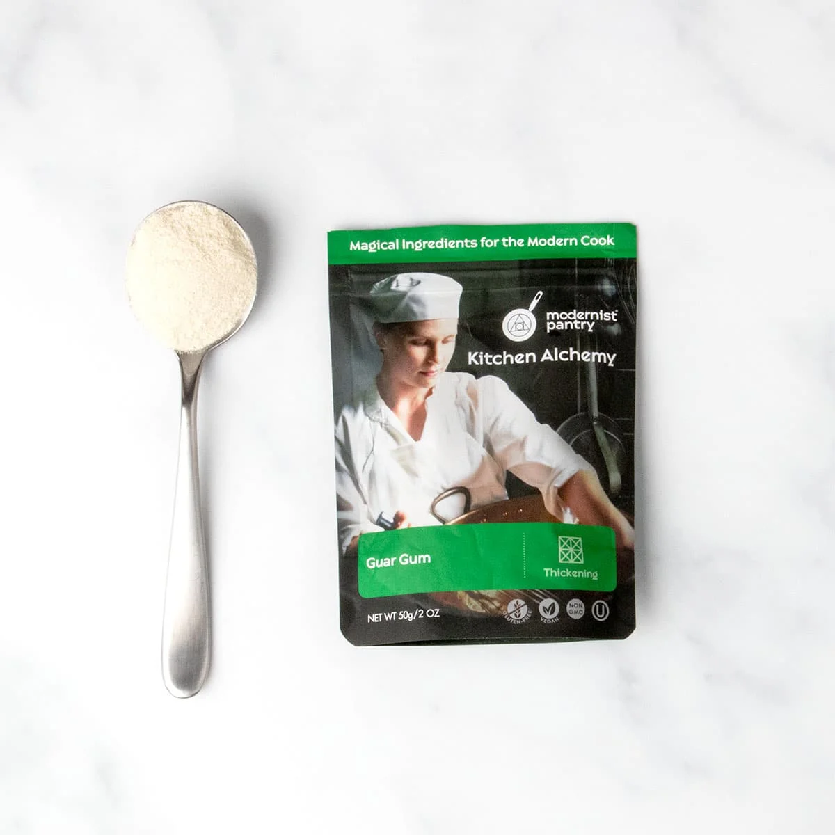 black and green pouch of guar gum with sample of white powder on large metal spoon