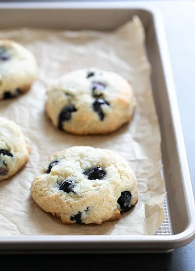 blueberry muffin tops on a baking tray lined with brown paper