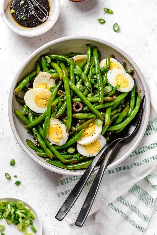 Bowl of green bean salad with hard-boiled eggs, olives, and scallions.