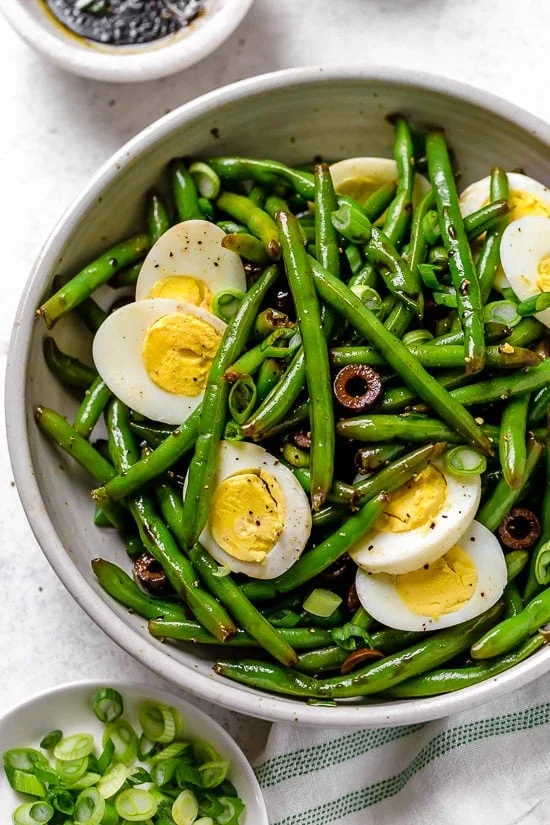 Bowl of green bean salad with olives and eggs.