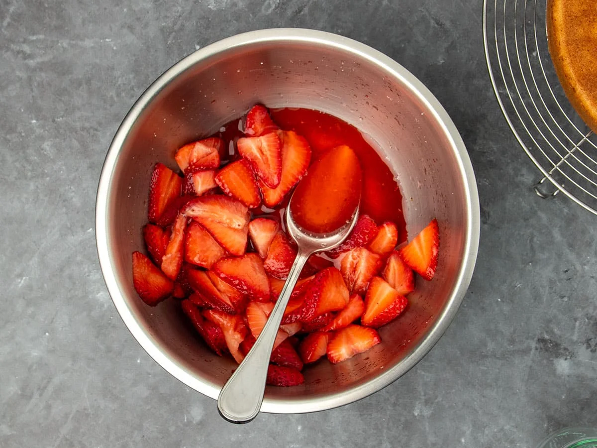 bowl of sliced strawberries with red rendered juice in bowl and on metal mixing spoon