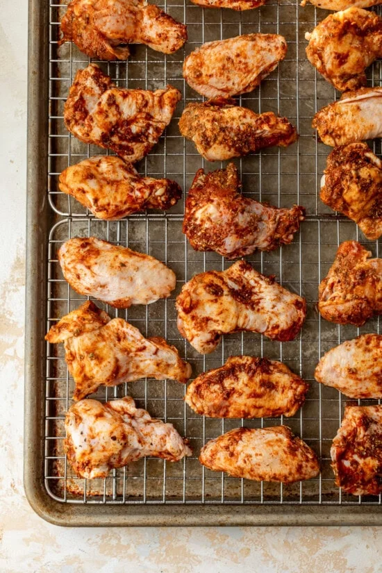 Broiled chicken wings on wire racks set on top of baking sheets.