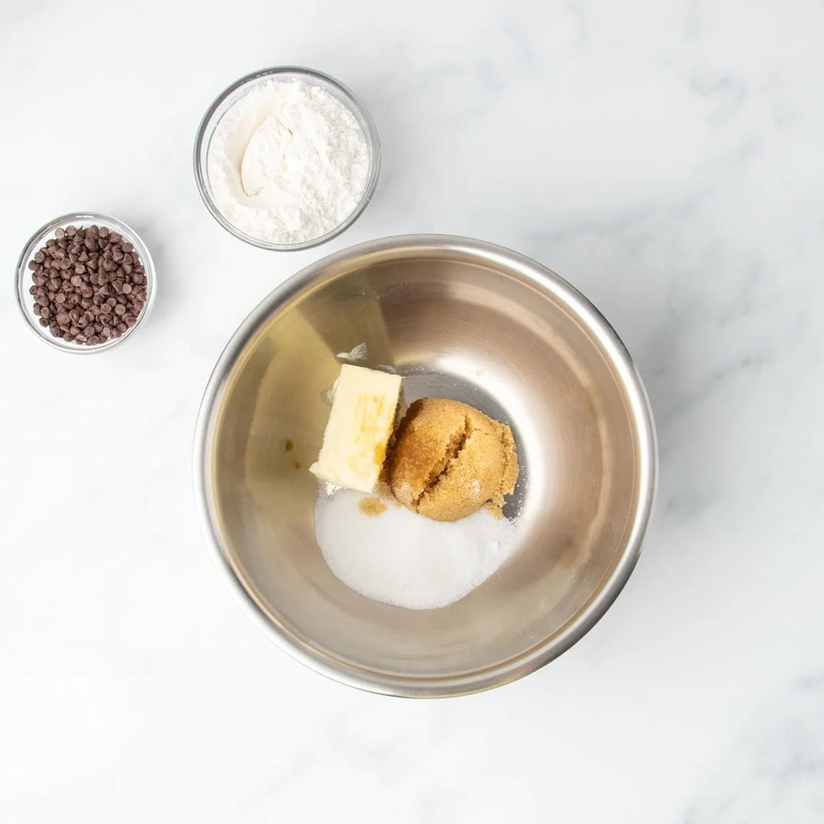 Brown and white sugars with butter in a metal mixing bowl, ready to be mixed for cookie dough.
