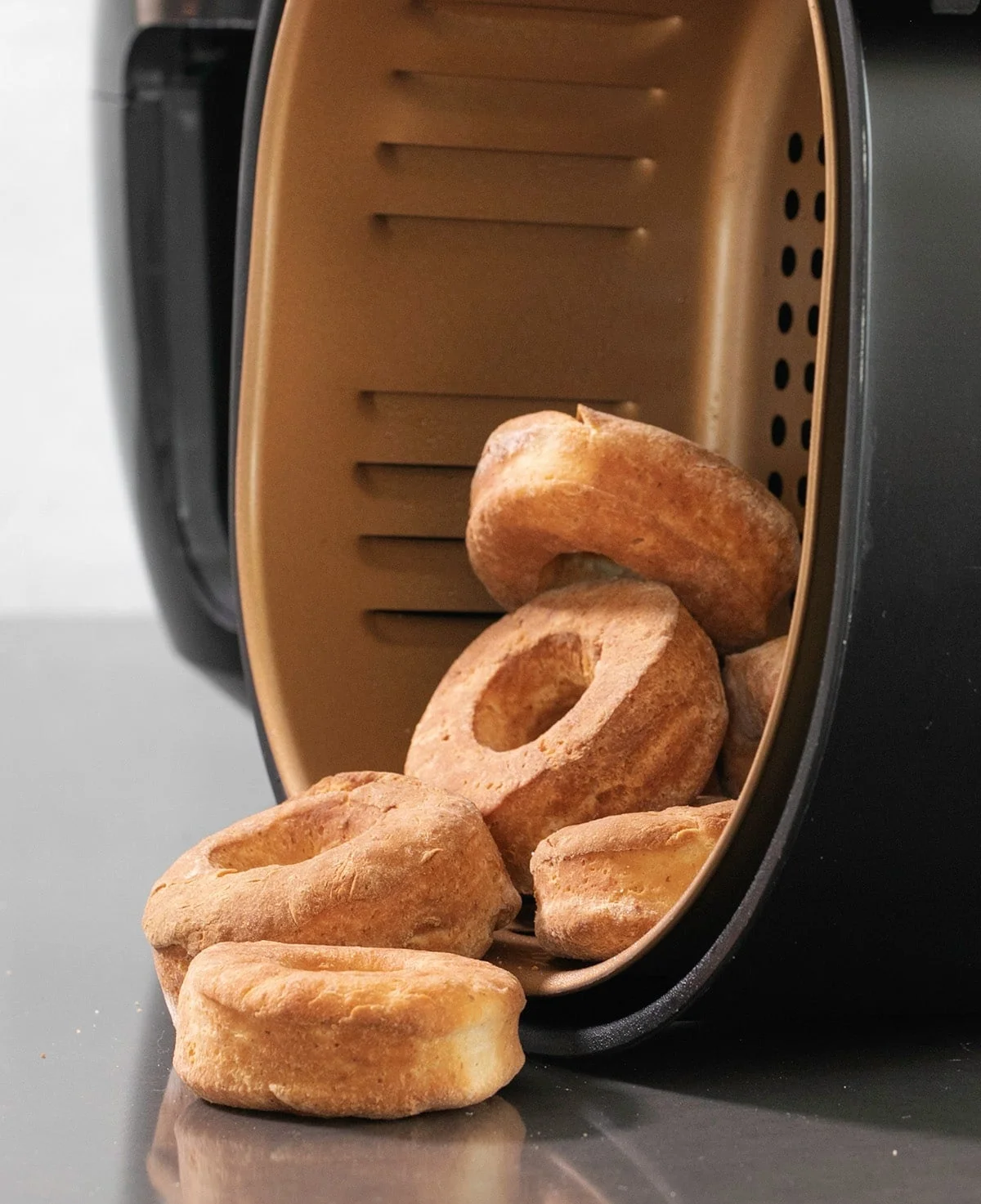 Brown baked donuts falling out of an air fryer basket turned on its side