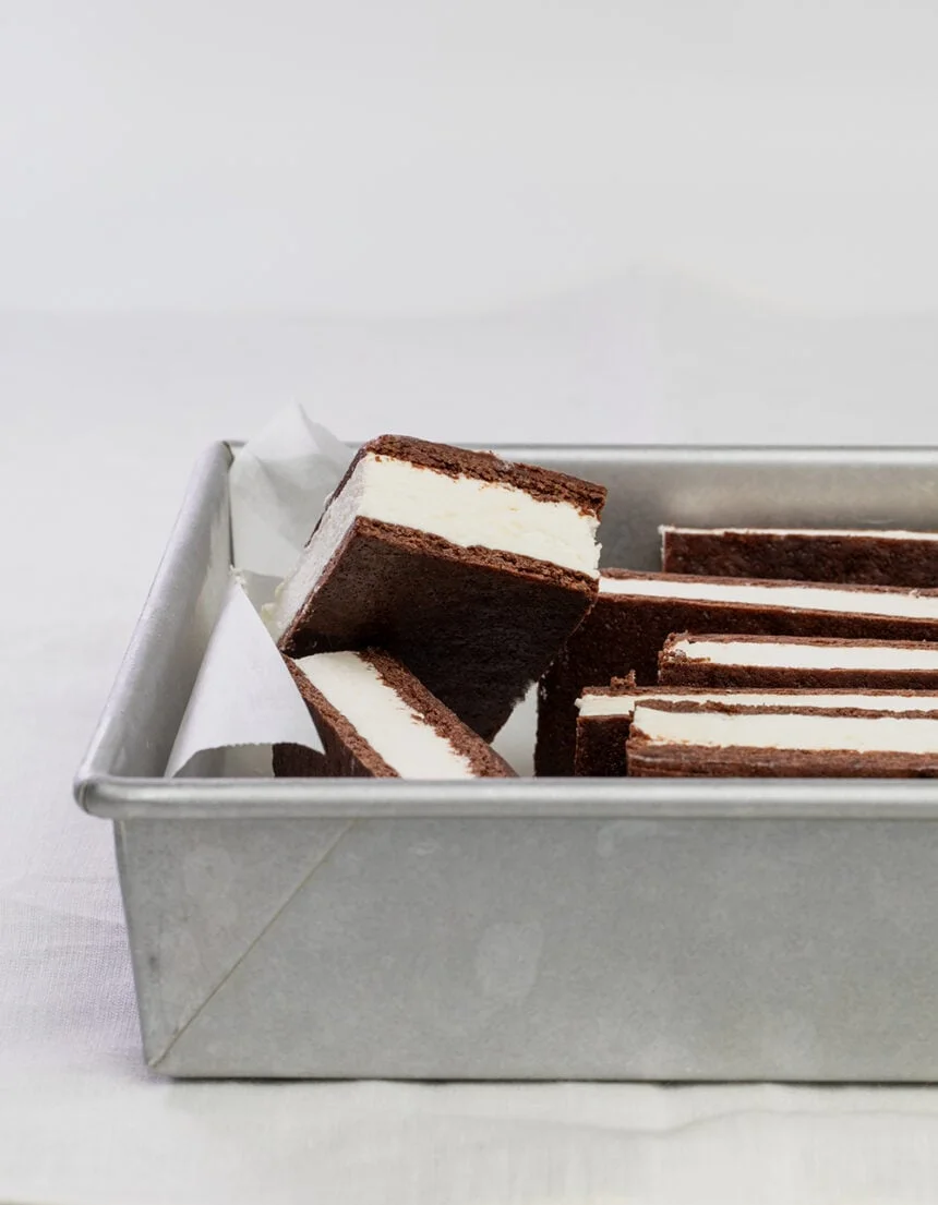 brown ice cream sandwiches with white ice cream piled in metal square baking dish with one sandwich sticking up
