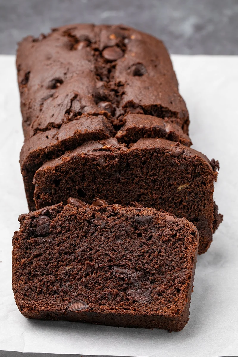 Brown quick bread loaf sliced 3 times on white paper.