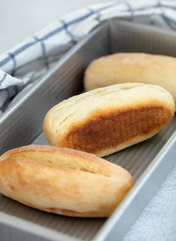 Buns in rectangular metal pan with blue and white checked tea towel.