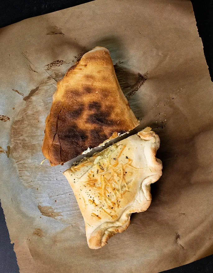 Calzone cut in half on brown paper with one part facing bottom up