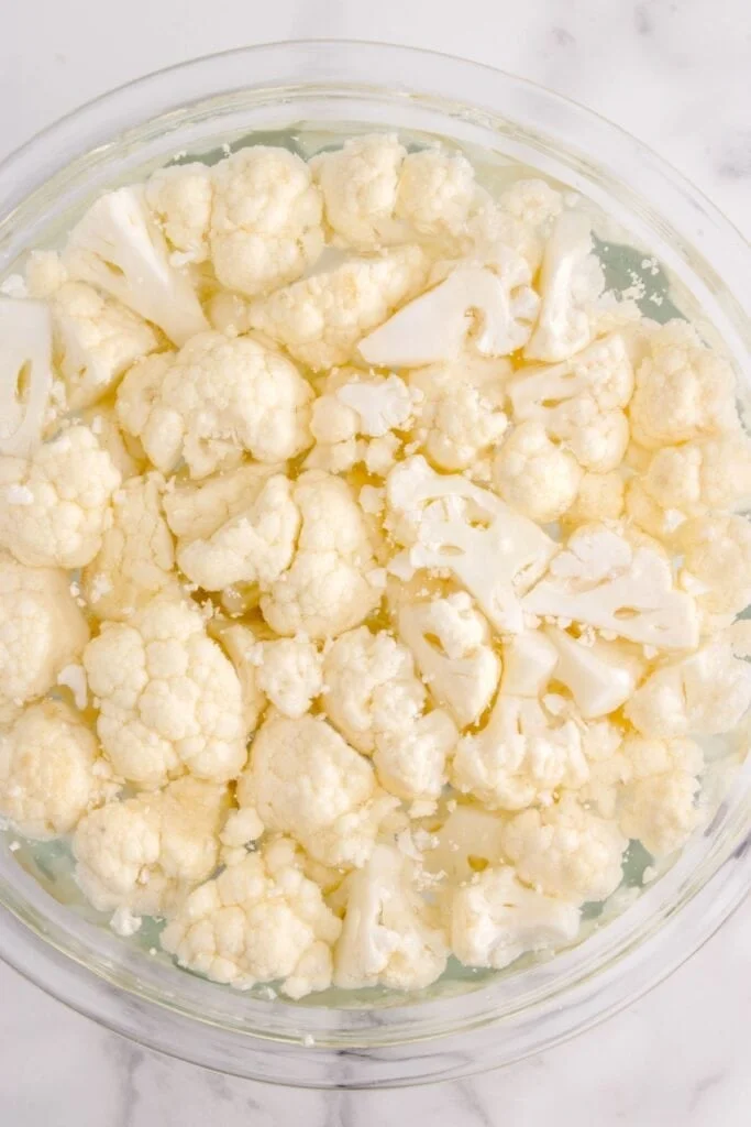 Cauliflower being cleaned in a glass bowl with water.