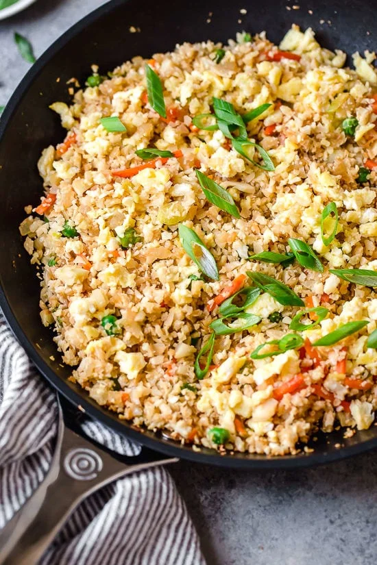 Cauliflower fried rice in skillet with vegetables and eggs.