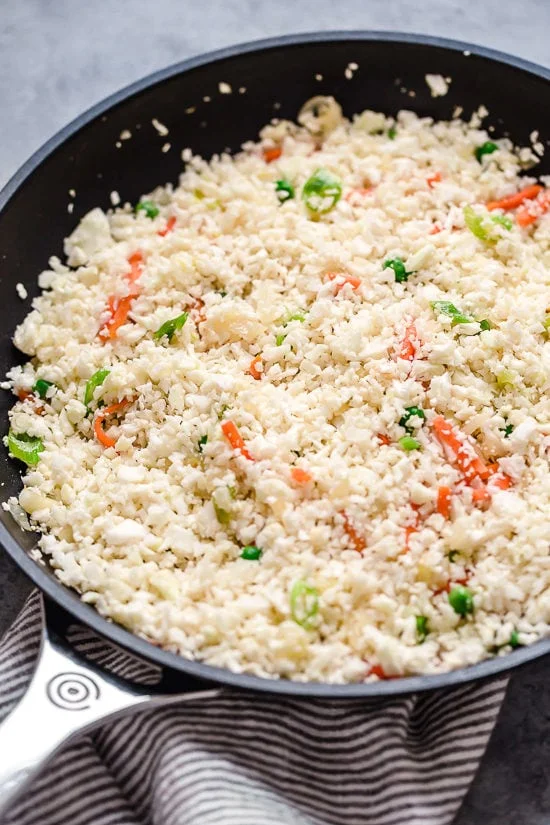 Cauliflower rice added to skillet with vegetables.