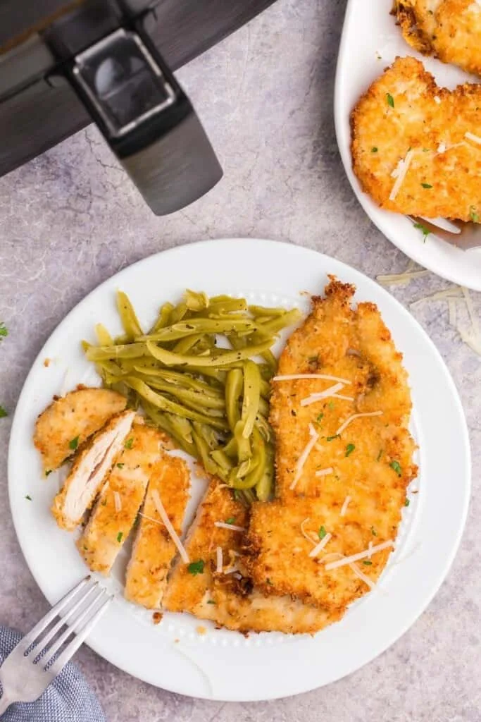 cheese crusted chicken on a plate with green beans 